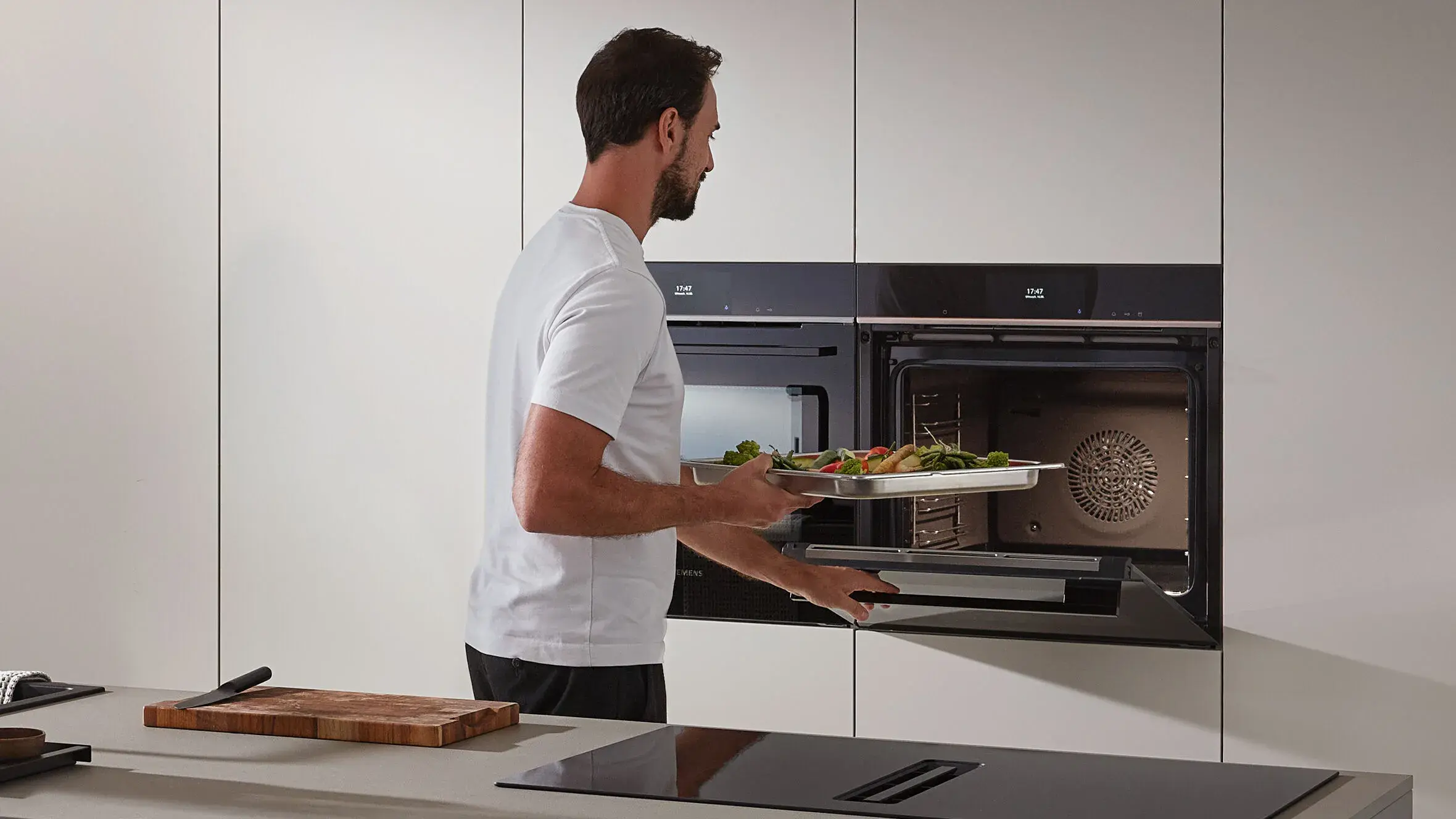 SIEMENS_Dampfgarer Mann mit Bart stellt Blech mit Gemüse in den Dampfgarofen